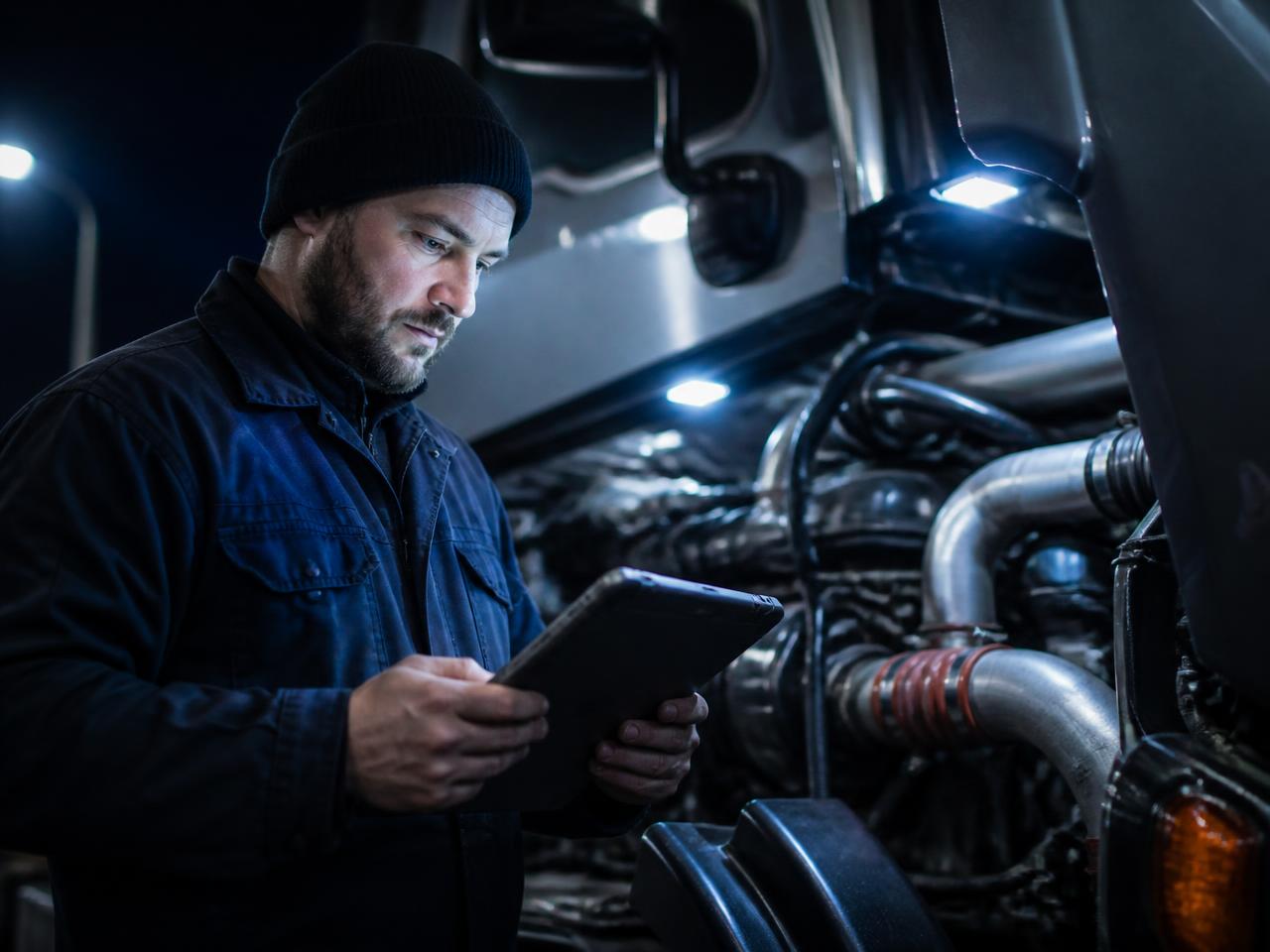 Technician reviewing predictive alerts on a tablet at a truck engine bay
